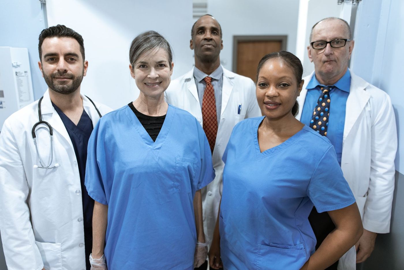 A team of five clinicians in scrubs and white coats