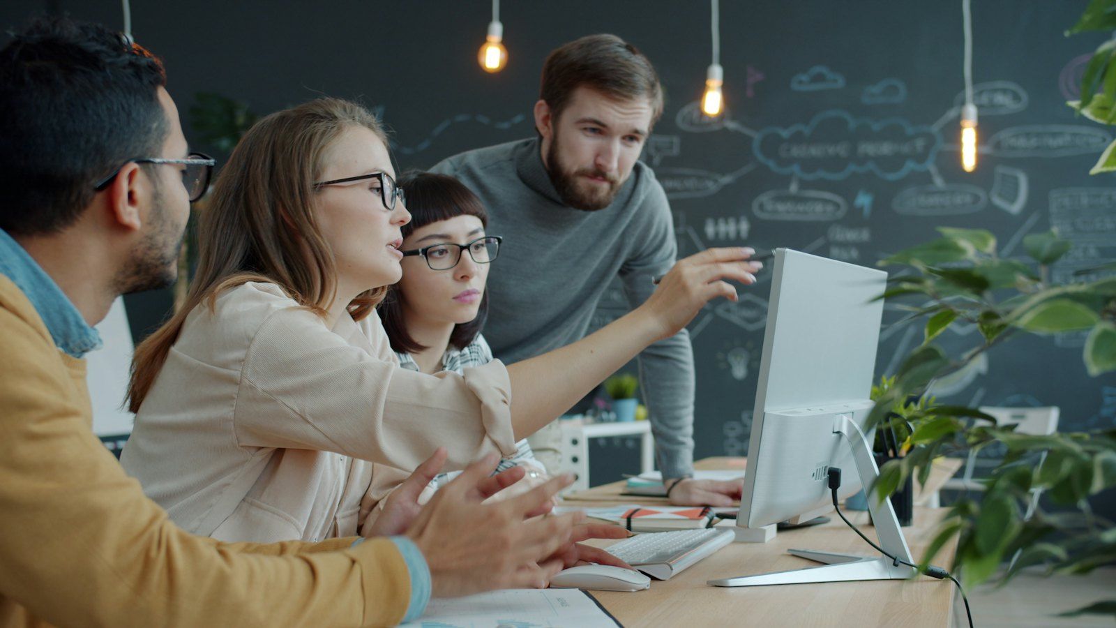 Four colleagues discussing work around a desktop monitor