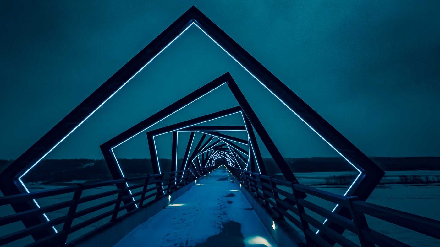 A footbridge running through a tunnel of square steel frames at dusk