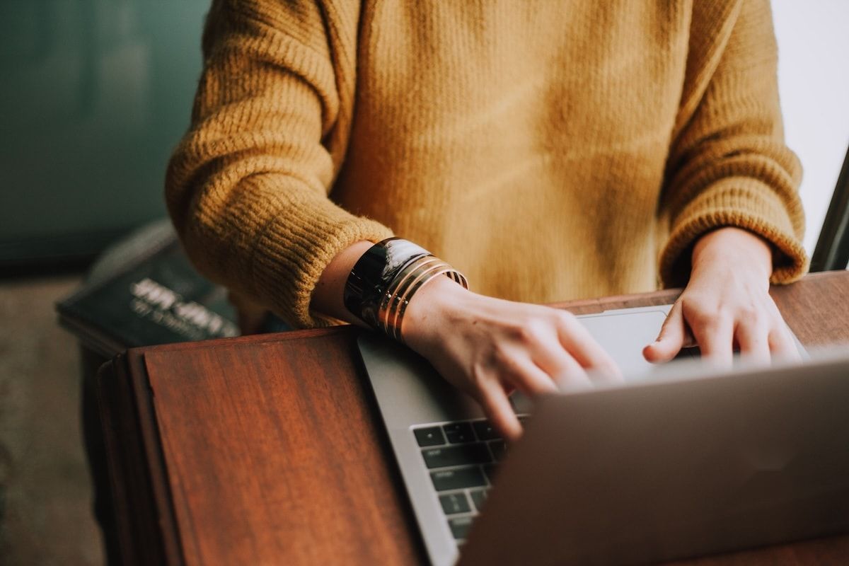 Someone typing on a laptop at a wooden desk at home