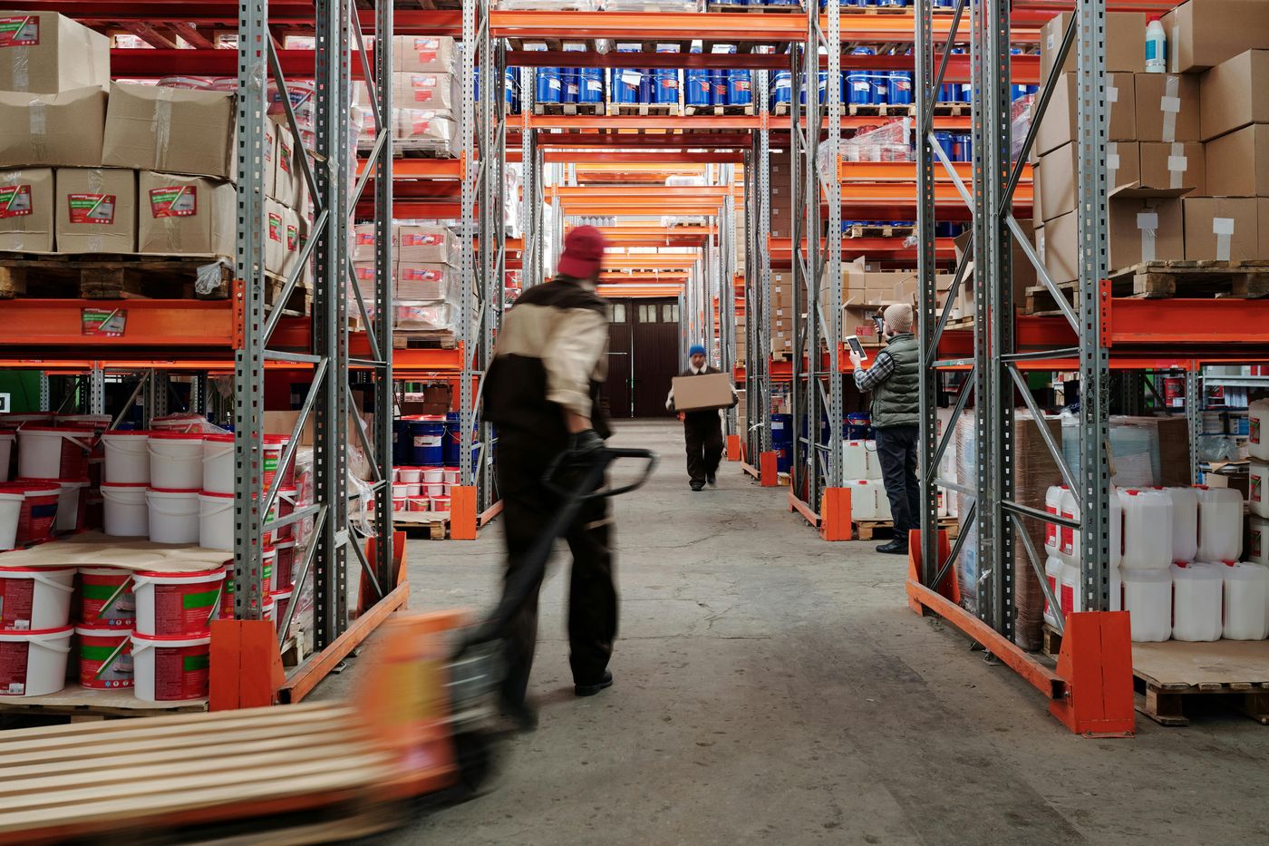 A warehouse aisle with orange racking and a worker moving a pallet